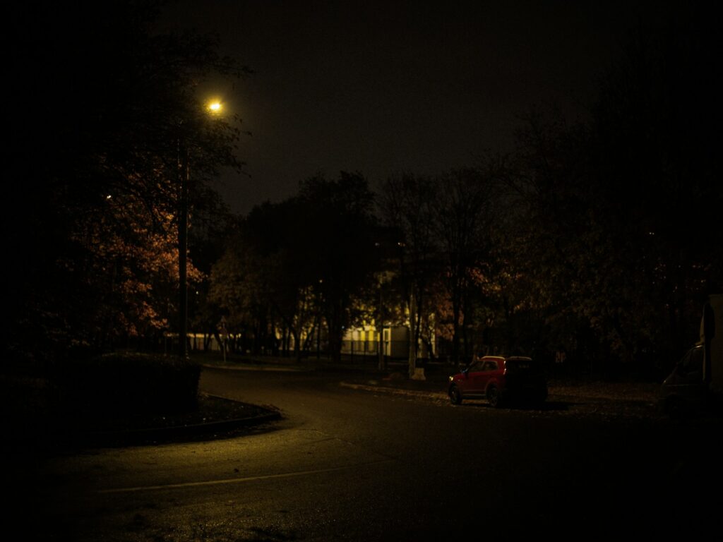 A car parked on a dark residential street at night, lit by a single streetlight.