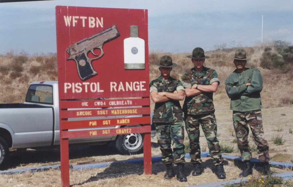 Marine Corps WFTBN Pistol Range sign listing PMI Sgt Rader, with three Marine instructors standing beside it