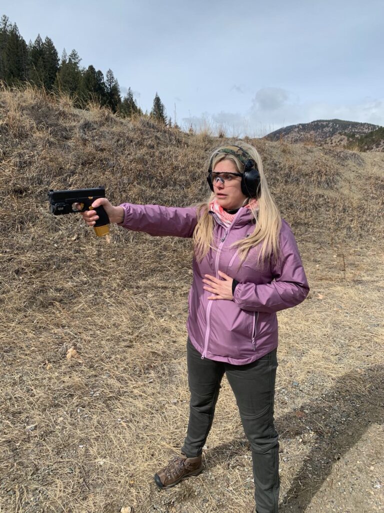 Woman practicing a two-handed pistol grip at an outdoor Colorado range